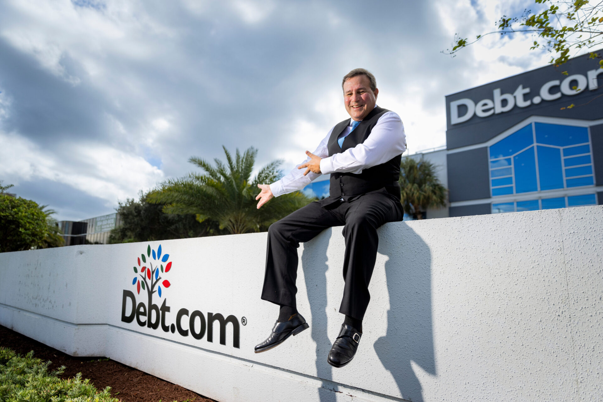 Howard Dvorkin sitting on ledge in front of Debt.com building and sign