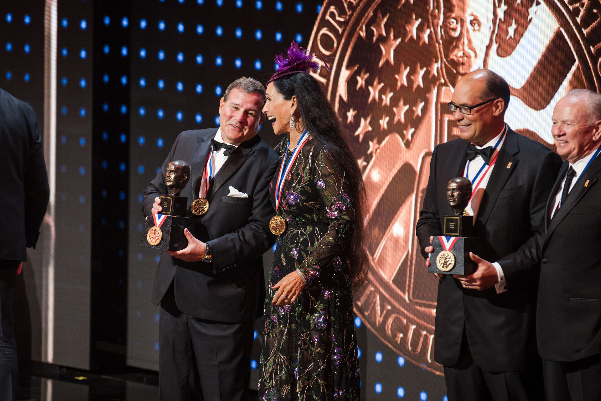 Howard Dvorkin receiving the Horatio Alger Award on stage, holding the bronze bust and medal while congratulating fellow honorees during the formal ceremony.