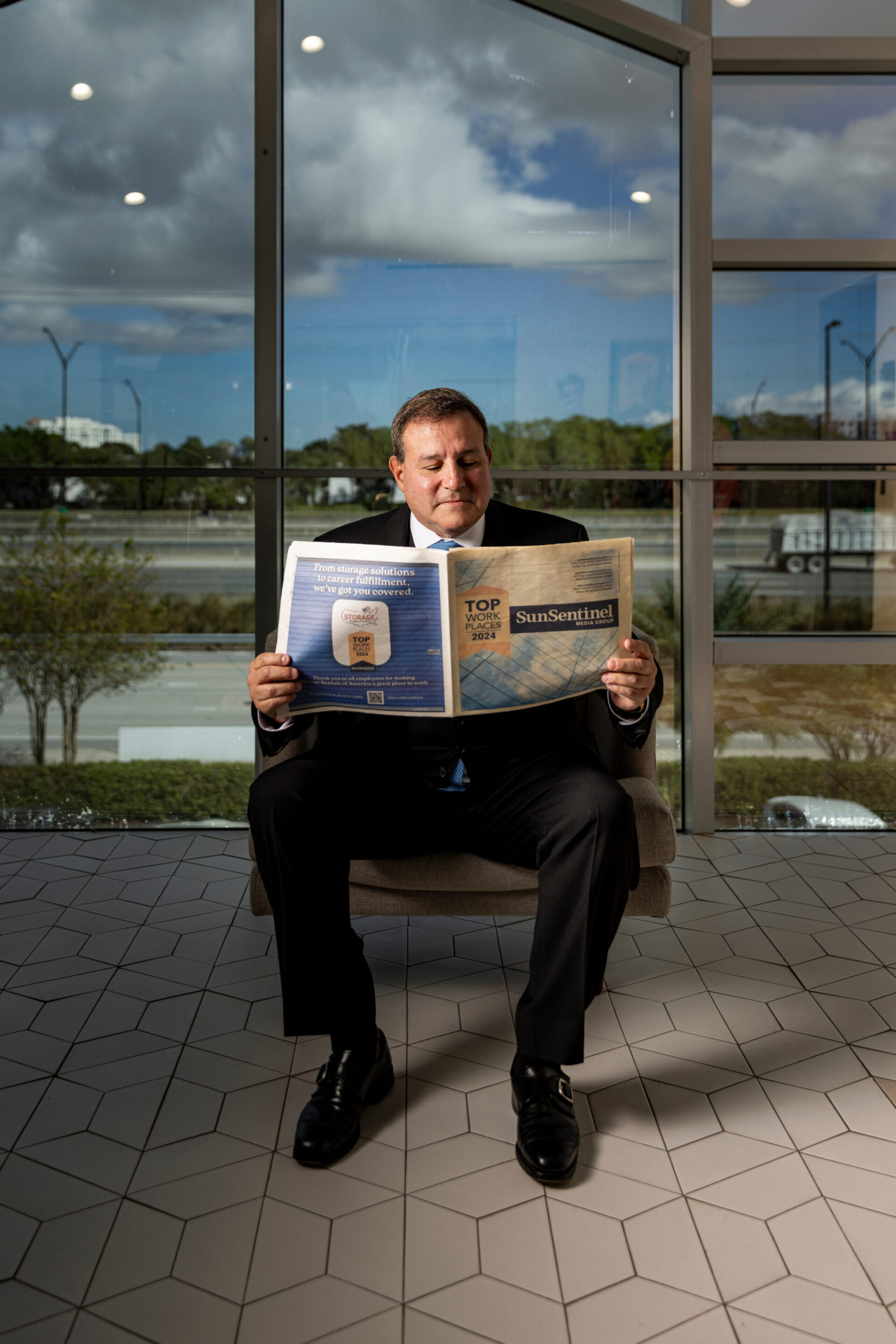 Howard Dvorkin leading a team meeting in a modern office, standing at the head of a conference table while colleagues listen and engage, with the Debt.com website visible on a screen behind him.